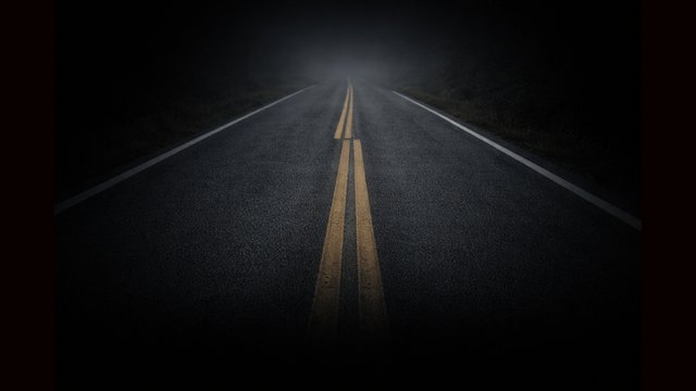 A dark two-lane road stretching into the distance